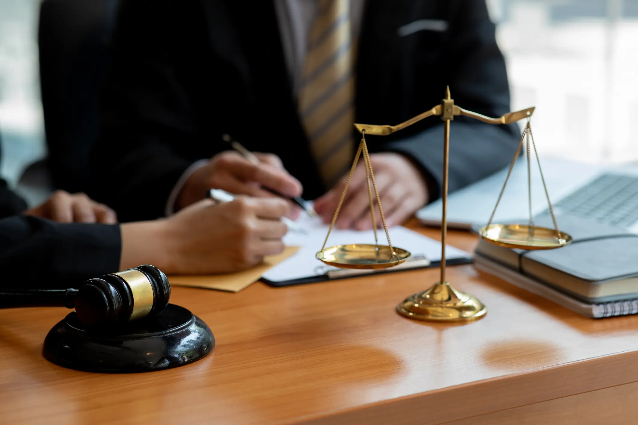 A judge writing notes with scales of justice and gavel on desk.